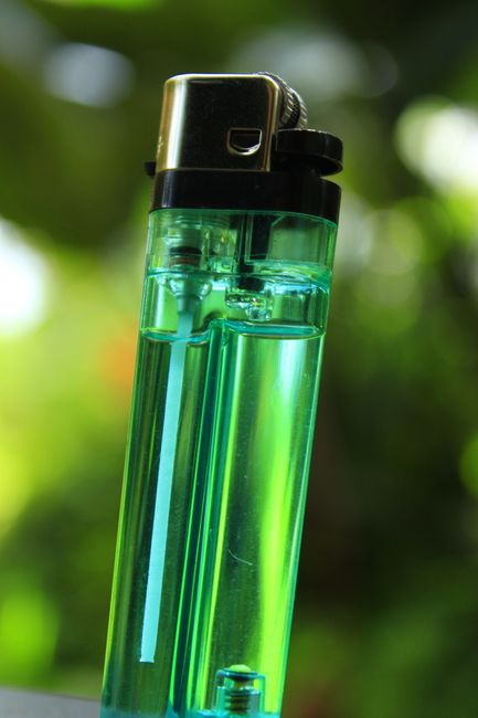 A detailed shot of a green transparent plastic lighter with a blurred natural background.