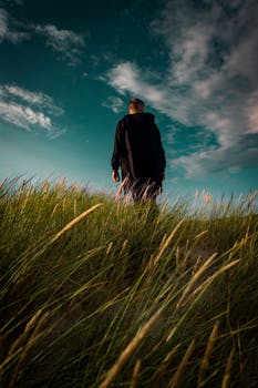 一个孤独的男人走过郁郁葱葱的草地，在充满活力的天空下捕捉到宁静