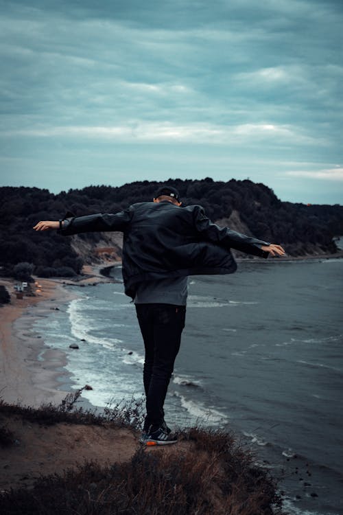 Man Standing On Cliff Facing Body Of Water