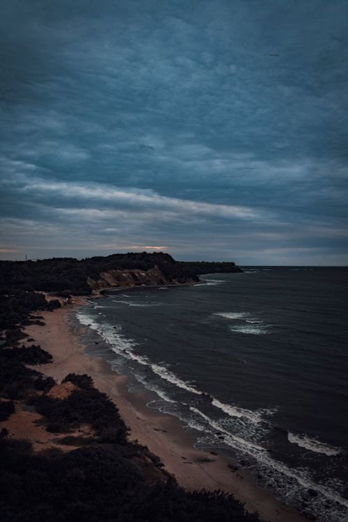 Free A moody seascape with dramatic cliffs and a peaceful beach under a cloudy sky. Stock Photo