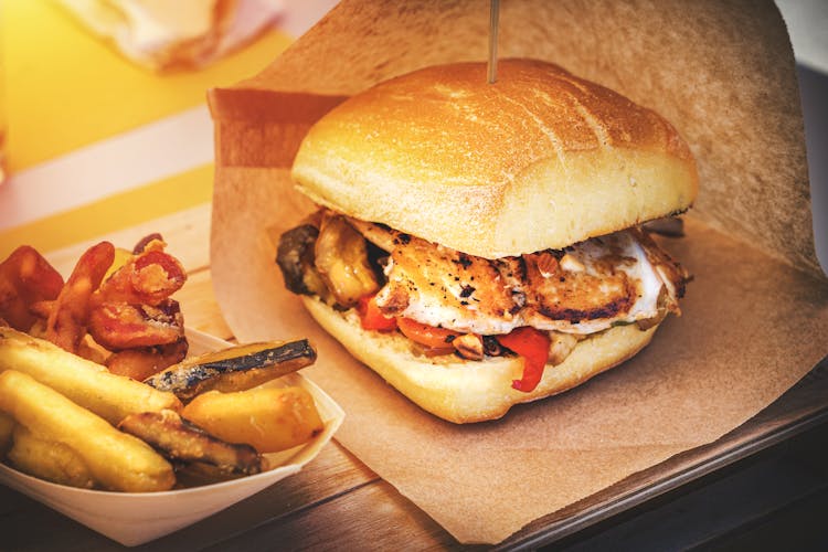 A Burger In A Brown Paper Bag And Potato Wedges In A Container