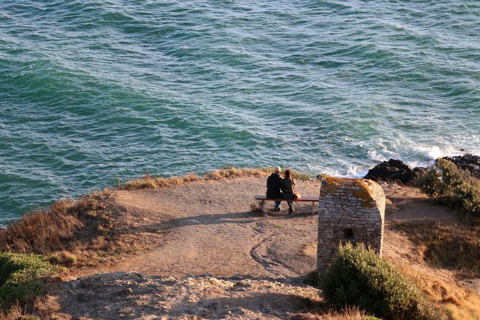 Couple sitting on a bench at cliff edge overlooking the ocean in Granville, Normandie, France.