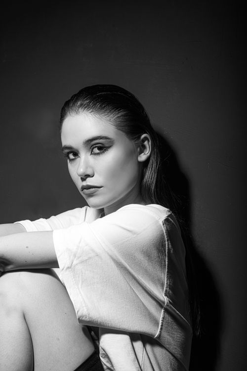 Free Artistic black and white portrait of a serious woman in a white shirt sitting against a dark background. Stock Photo