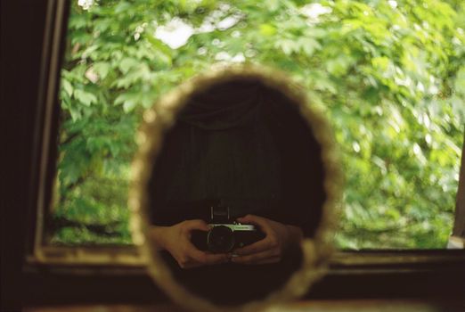 A vintage style photo capturing a reflection of a photographer holding a camera amidst lush greenery.