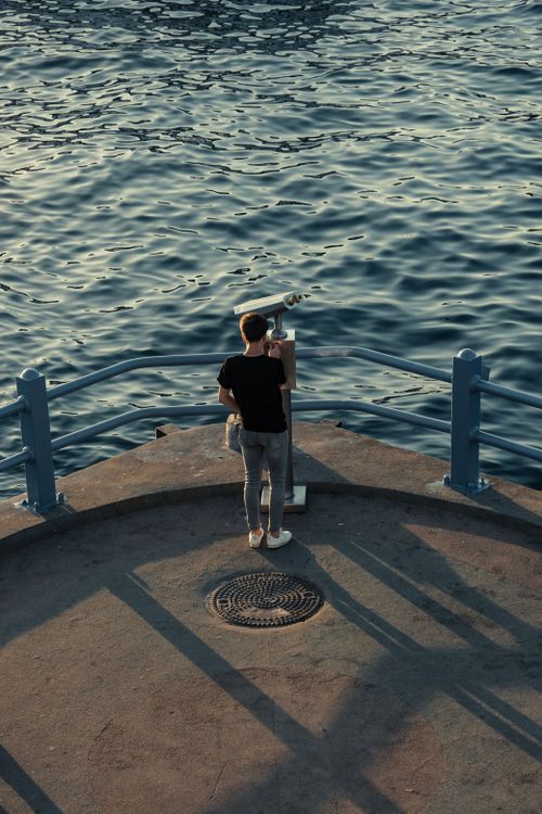Free A person on a dock looking through binoculars at sunset over the water. Stock Photo