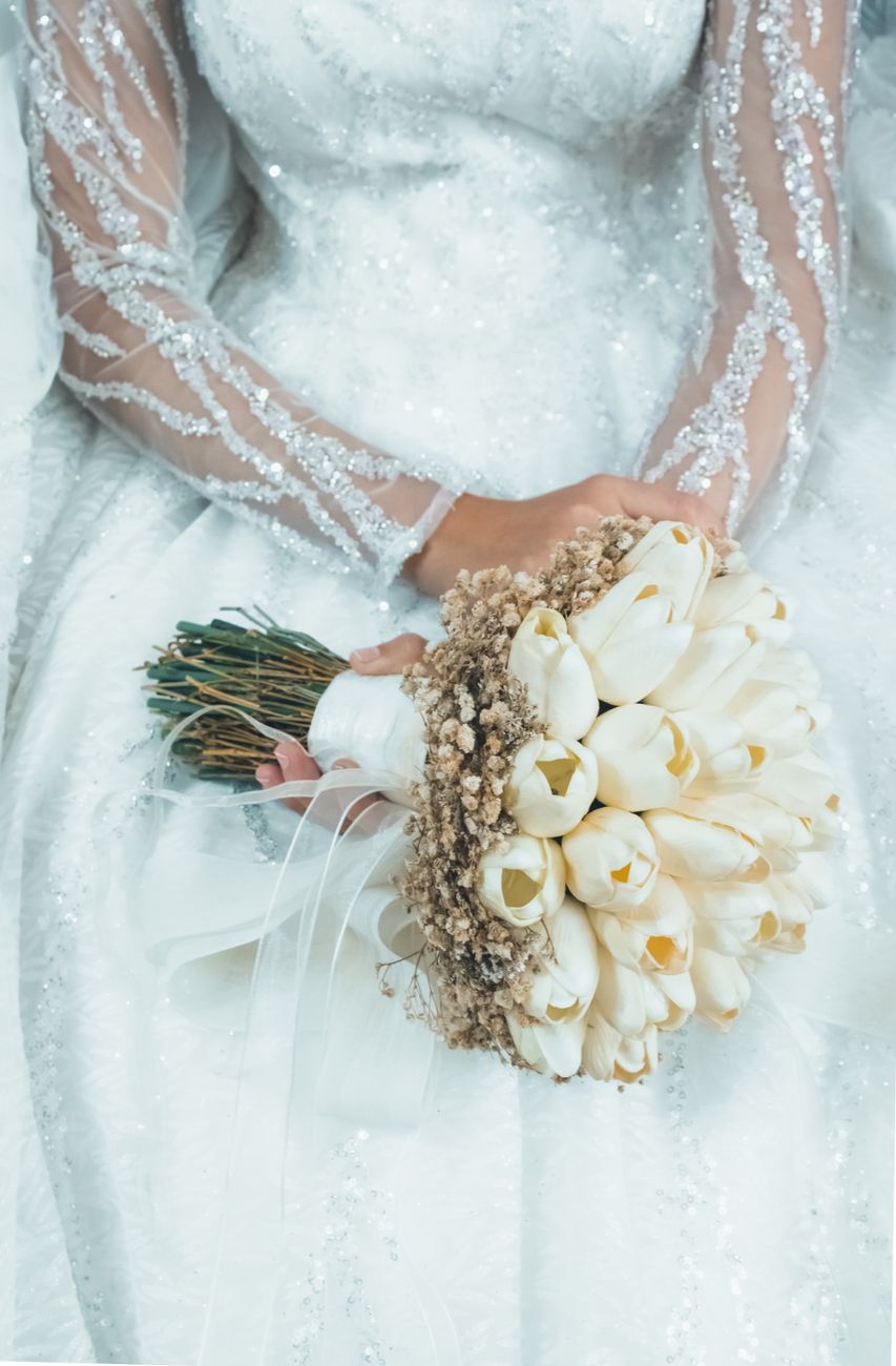 An elegant bride holding a bouquet of white tulips in a detailed wedding gown.