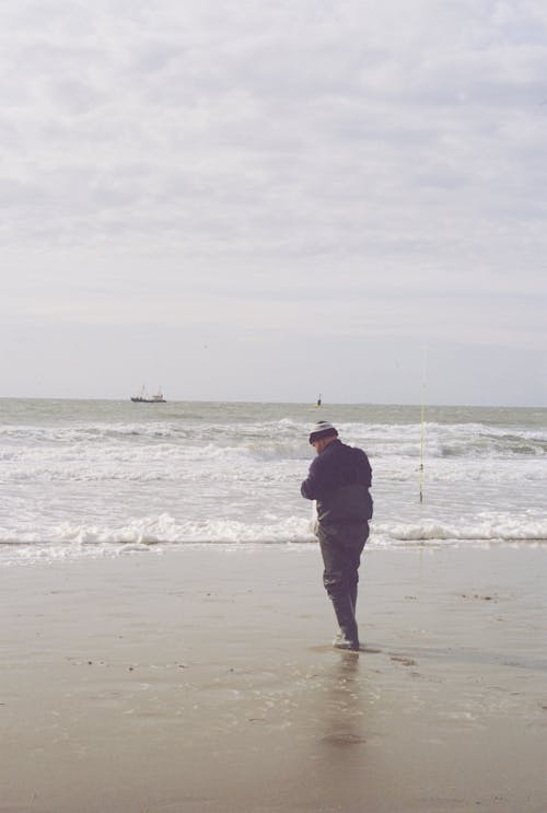 A Man in Black Jacket and Pants Standing on the Beach