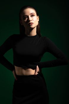 Elegant female model posing confidently in a black outfit with dramatic studio lighting.