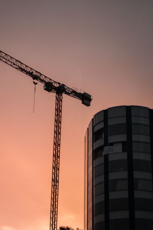Free Silhouette of a tower crane and building against a vibrant sunset sky. Stock Photo