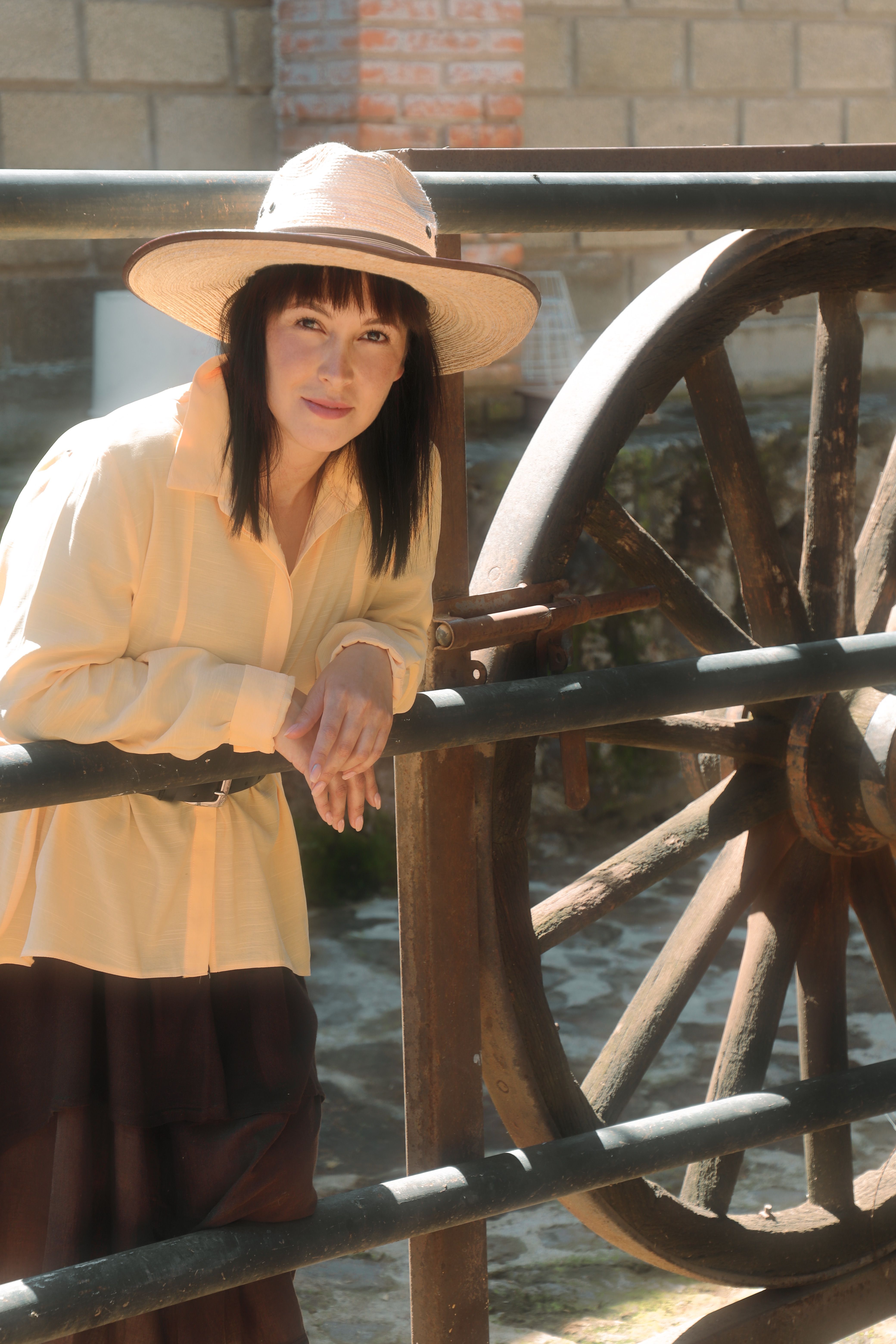 Woman in a sun hat next to a traditional wooden wheel in Mexico City.