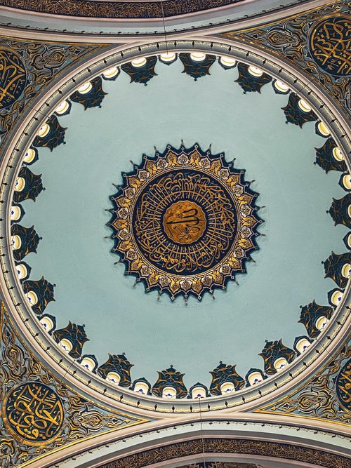 Free Upward view of an ornate mosque dome showcasing intricate Arabic calligraphy and detailed mosaic design. Stock Photo