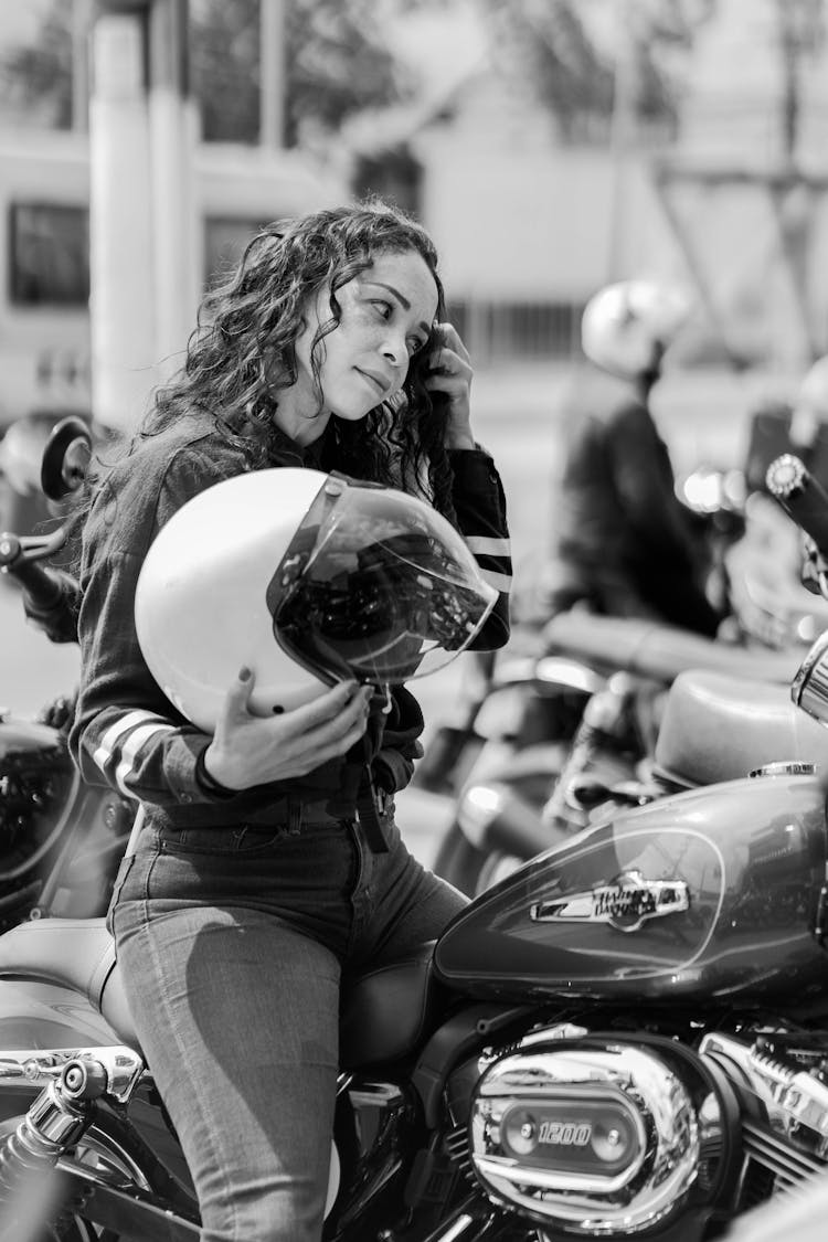 Grayscale Photo Of Woman In Black Jacket Holding White Helmet While Sitting On Motorcycle