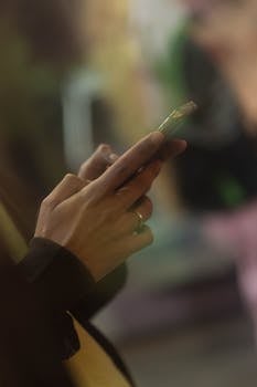 Person using a smartphone indoors, showcasing fingers and a blurry background.