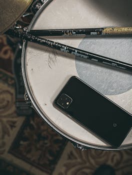 A smartphone and drumsticks placed on a drum, showcasing a musical setting.