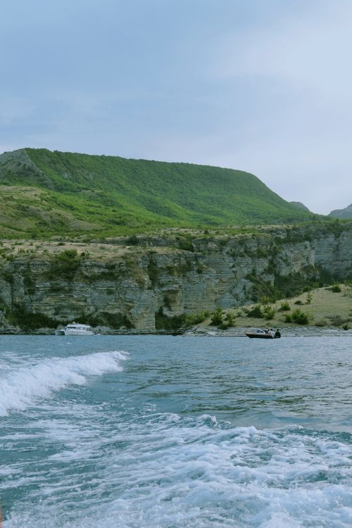 Free Serene view of a blue ocean with rocky cliffs and green hills under a calm sky. Stock Photo