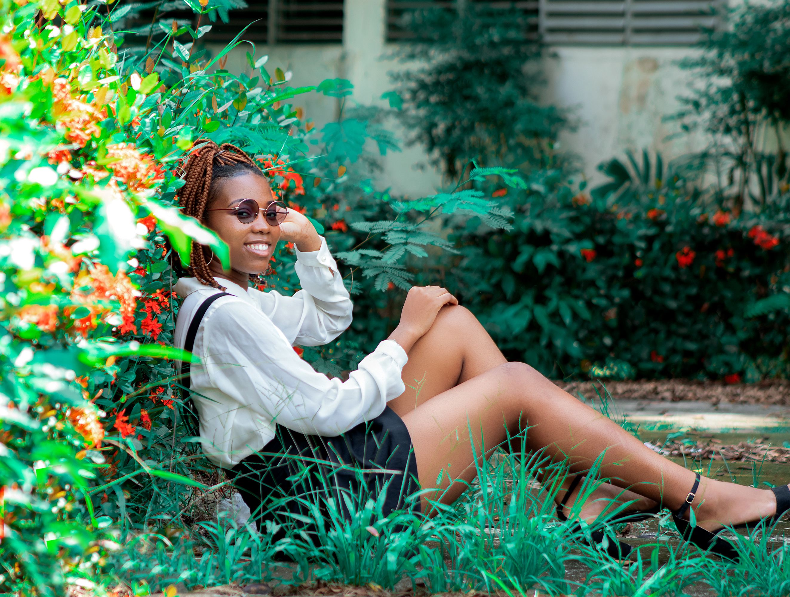 A cheerful young woman with braids and sunglasses enjoying a peaceful garden setting on a sunny day.