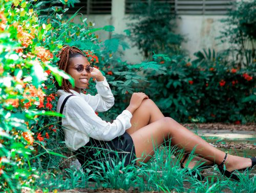 Free A cheerful young woman with braids and sunglasses enjoying a peaceful garden setting on a sunny day. Stock Photo