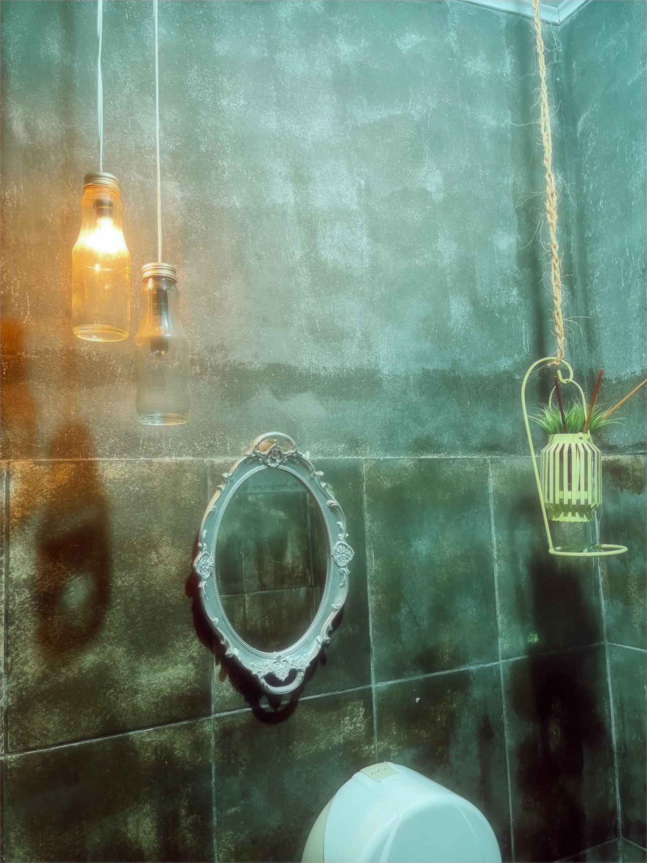 Two amber glass bottle pendant lights hanging beside a vintage oval mirror in a farmhouse style bathroom