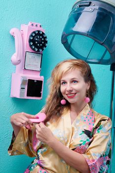 Woman in vintage salon wearing kimono brushing hair near retro pink telephone.