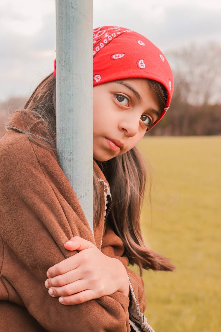 Girl In Red Bandana And Brown Coat Holding Gray Metal Pole