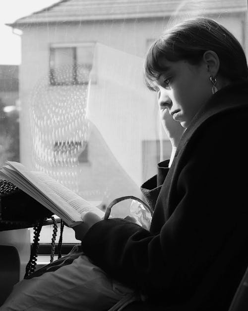 Grayscale Photo of a Woman Reading a Book while Riding a Bus