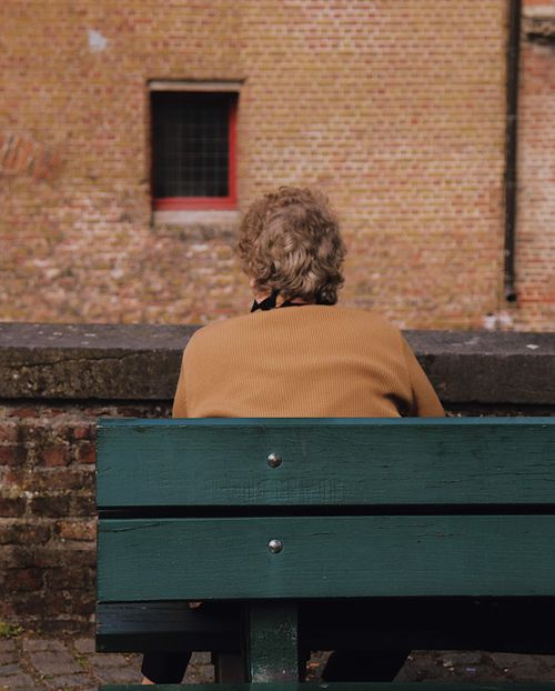 Free A woman sits alone on a park bench with a brick wall in the background. Stock Photo