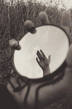A hand reflected in a small outdoor mirror, emphasizing a grayscale artistic tone.