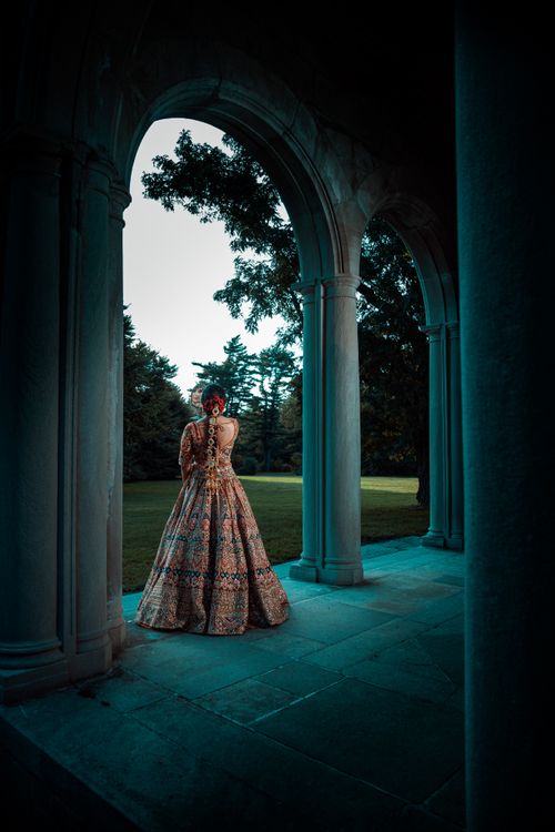 Free A bride in an elaborate lehenga stands gracefully under an archway outdoors. Stock Photo