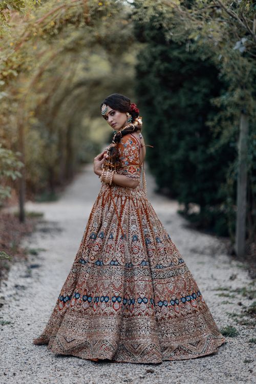 Free A young bride in a traditional ornamented dress stands gracefully outdoors, surrounded by lush greenery. Stock Photo