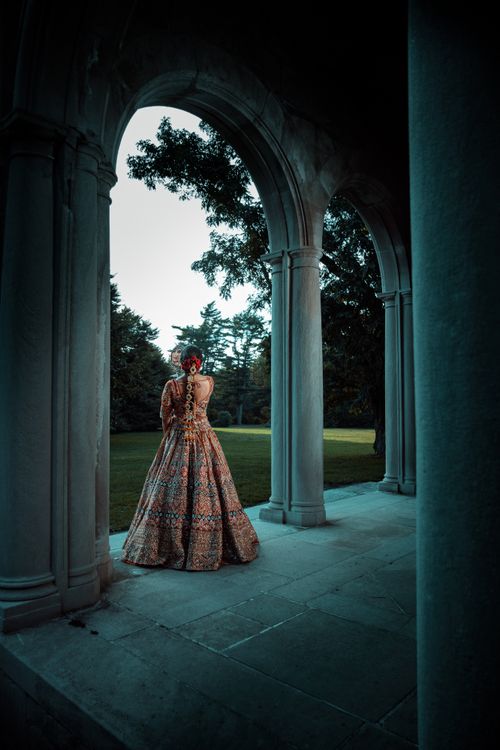 Free Elegant woman standing under stone arches in a vintage gown, creating a timeless and mysterious scene. Stock Photo