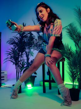 Fashionable young woman posing indoors with colorful lighting and potted plants, holding a camera.