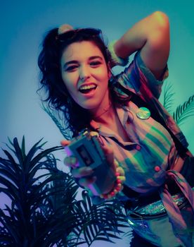 Young woman enjoying music and dancing with a retro cassette player in a vibrant scene.