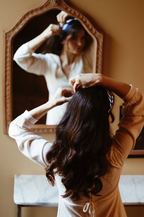 Woman Fixing Her Hair in Front of the Mirror