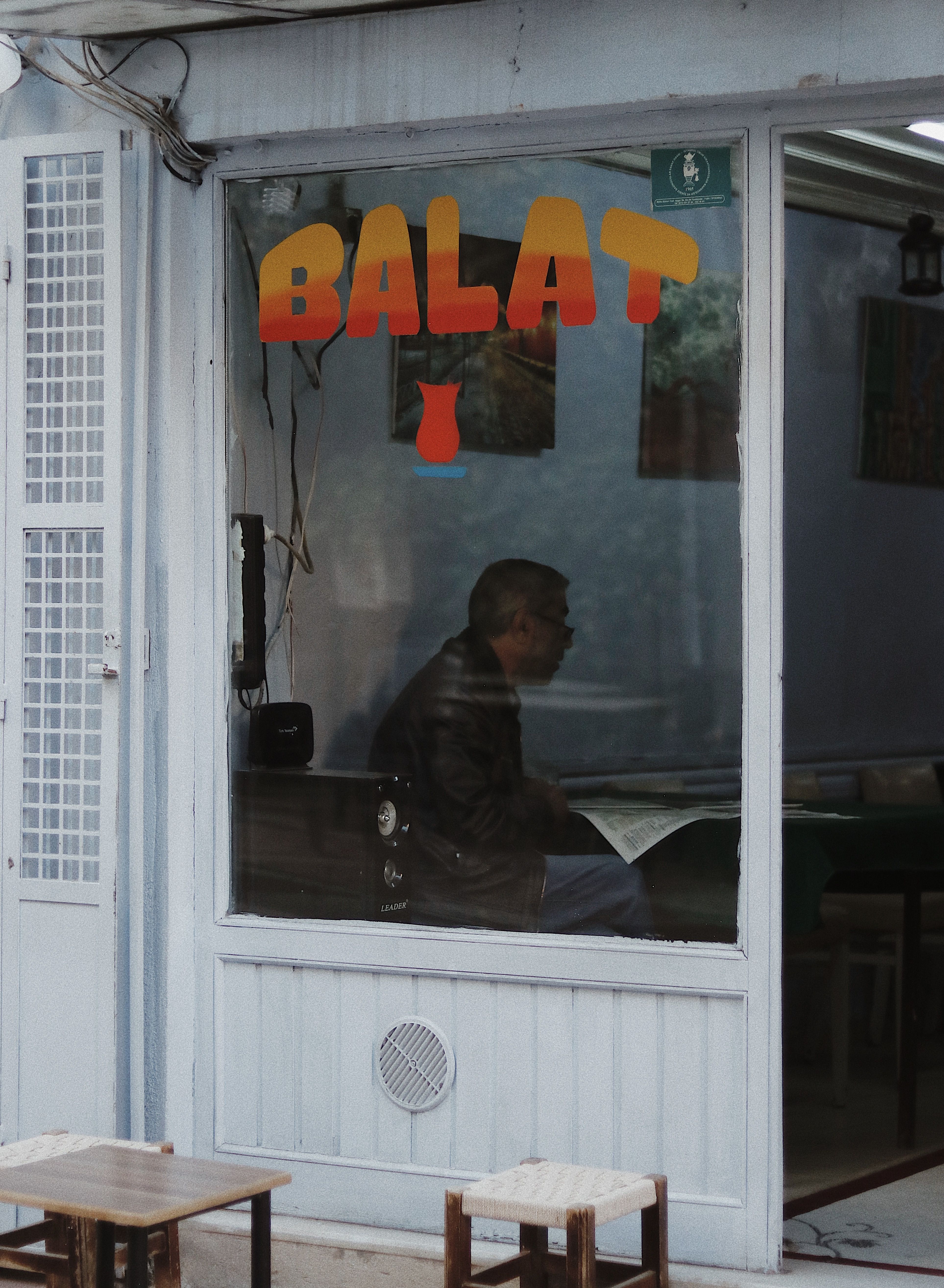 A cozy café in Balat featuring a customer reading inside, captured through a large window.