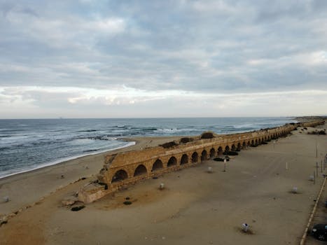 Scenic view of Caesarea's historic Roman aqueduct by the sea under a cloudy sky. by Lio Voo