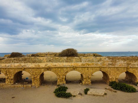 Discover the historic Roman aqueduct in Caesarea, set against a dramatic sky and serene seascape. by Lio Voo