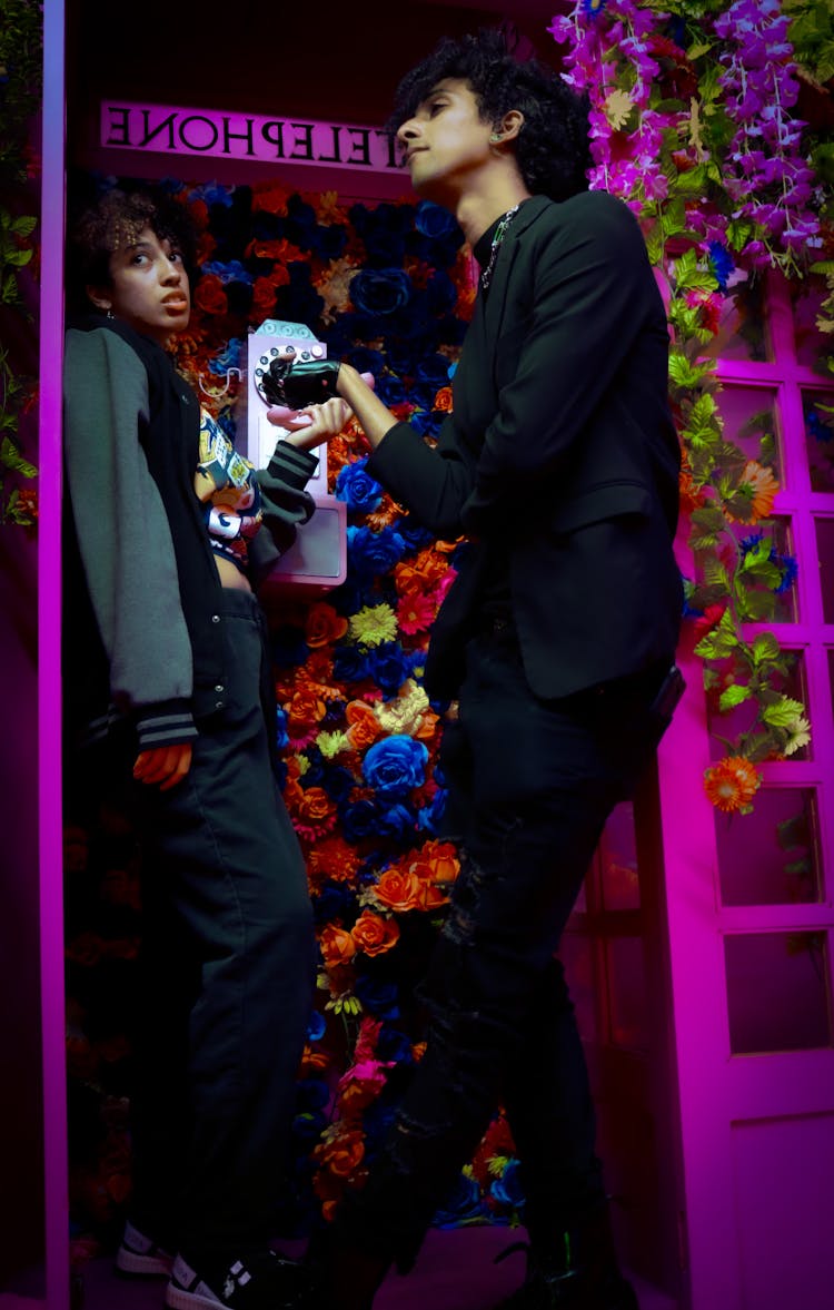 A Man And Woman Standing Inside The Telephone Booth With Flowers