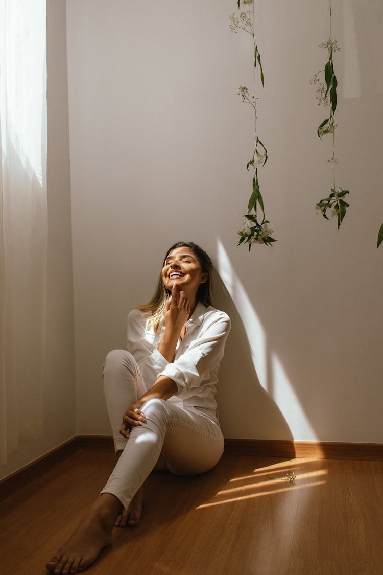 Smiling Woman Sitting On Floor At Home Near Flowers Decorations