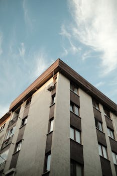 Low angle view of a modern building exterior with glass windows against a blue sky.
