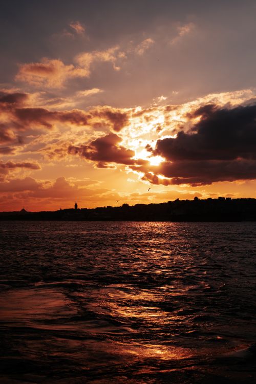 Free Vibrant sunset reflecting over water with silhouetted city skyline and dramatic clouds. Stock Photo