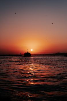 A breathtaking sunset casting warm hues over a silhouetted ship sailing on a calm sea.