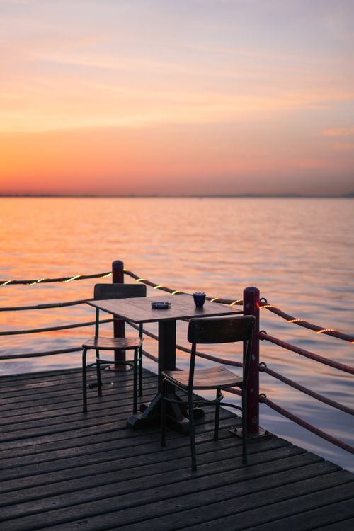 Free Serene sunset on a lakeside jetty with an empty table set for two, tranquil ambiance. Stock Photo