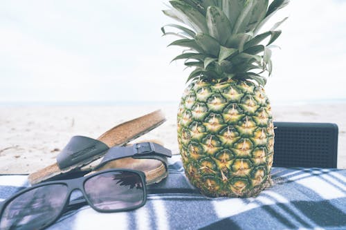 Black Framed Sunglasses Beside Slide Sandals and Pineapple