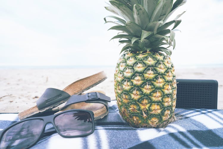 Black Framed Sunglasses Beside Slide Sandals And Pineapple