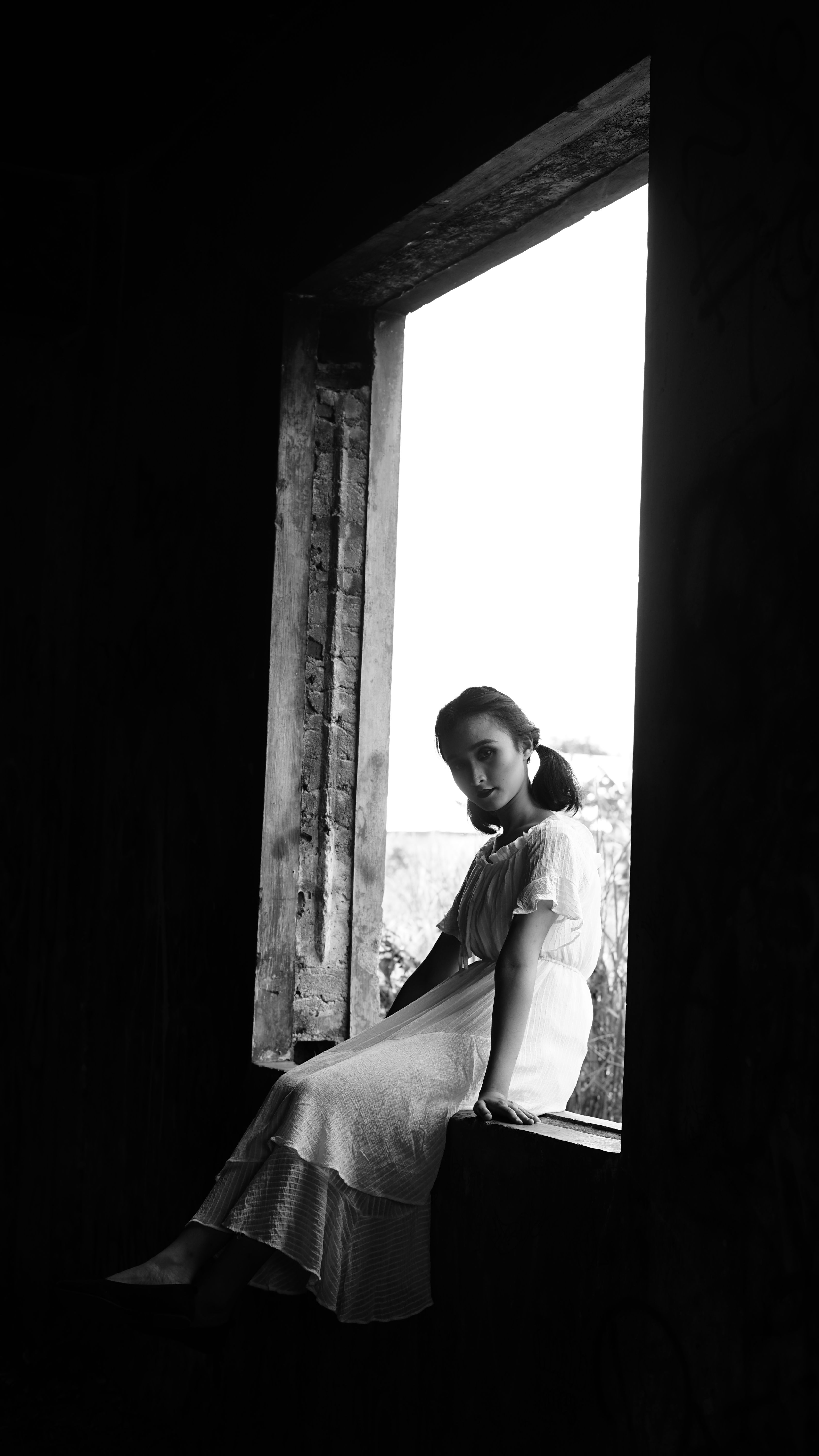 Grayscale Photo of Woman Sitting on the Window · Free Stock Photo