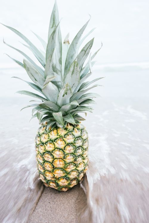 Free Fresh pineapple on a sandy beach with waves, symbolizing tropical freshness and summer vibes. Stock Photo