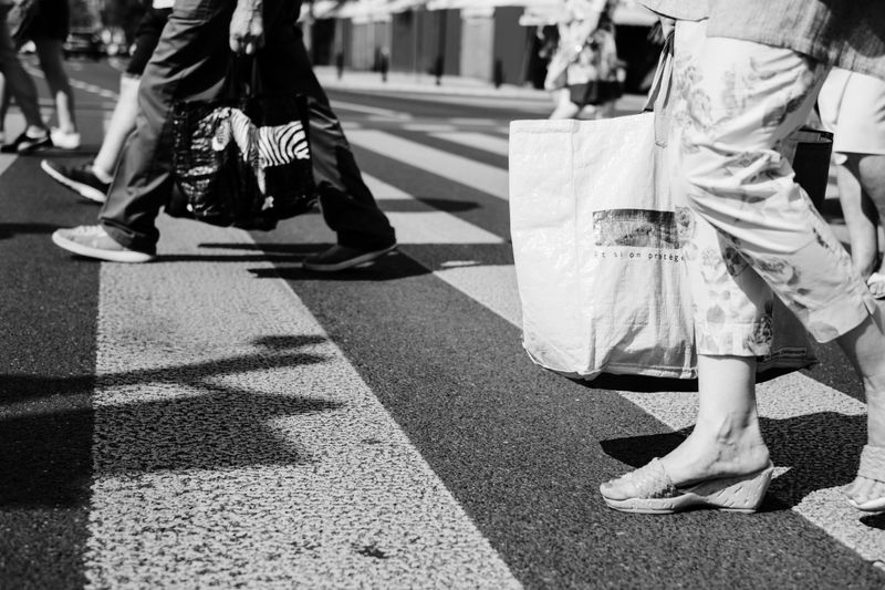 A monochrome image capturing diverse pedestrians walking across a crosswalk.