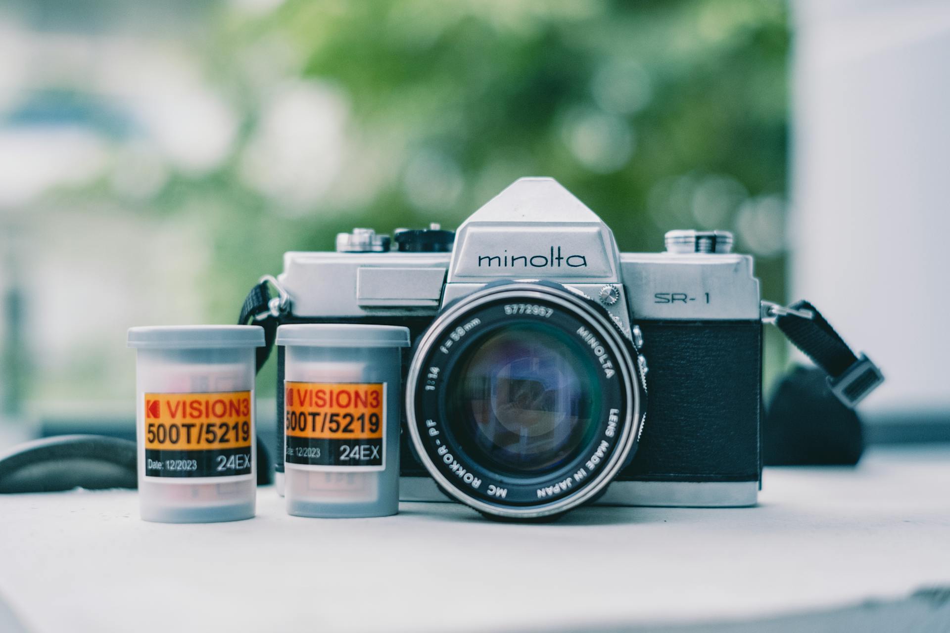 Close-up of Minolta SR-1 camera with Kodak Vision3 film rolls on white surface.