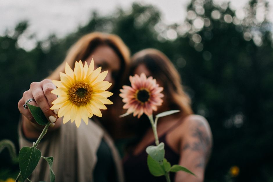 Two women holding sunflowers outdoors, showcasing nature's beauty.