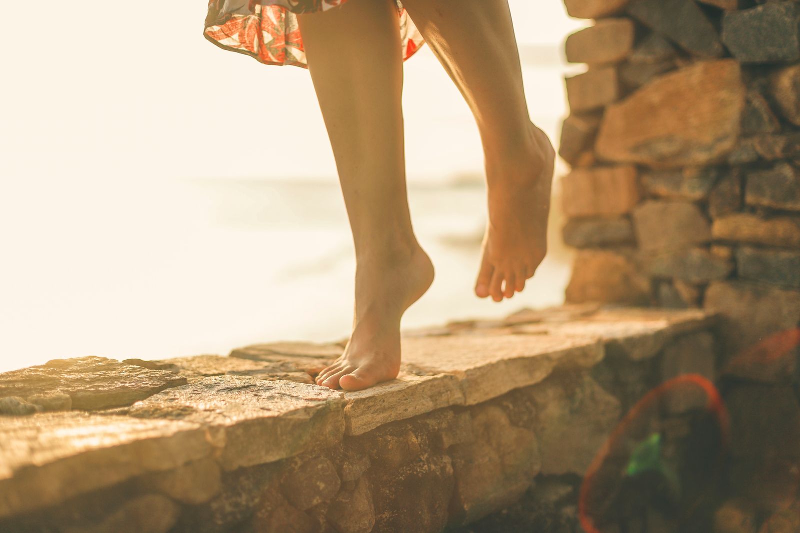 A woman balances barefoot on a stone wall by the sea during a serene evening in Weligama, Sri Lanka.